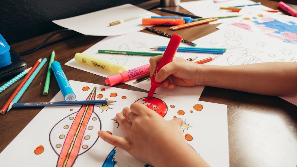 A child coloring a space-themed picture with colored pencils and markers on a desk.